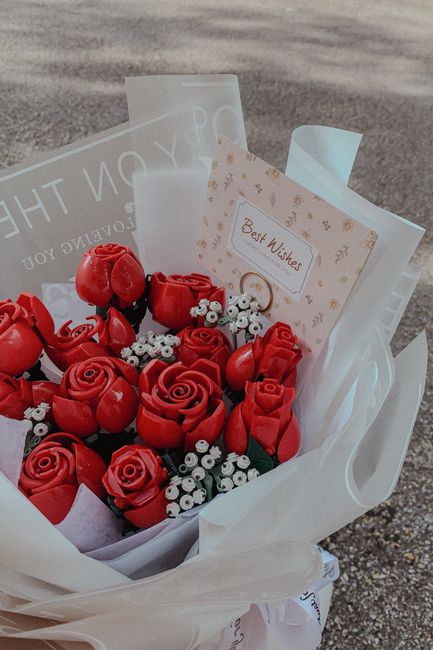 A bouquet arranged with vibrant red roses and small white filler flowers, wrapped in white tissue paper and clear cellophane, appears freshly made and ready for delivery. The flowers are positioned in